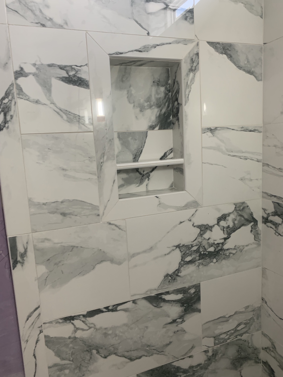 Large-format marble-look shower tile with a recessed niche and crisp grout lines
