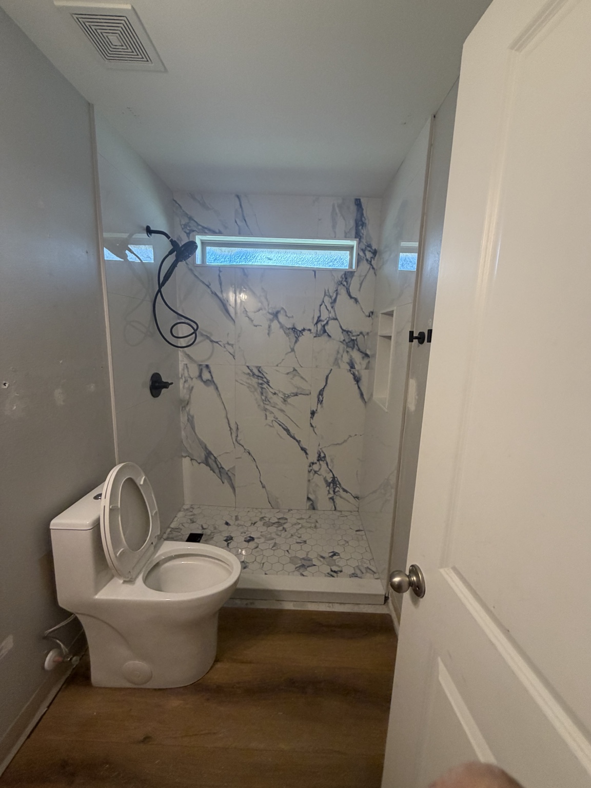 Finished walk-in shower with marble-look tile, recessed niche, black fixtures, and a high window
