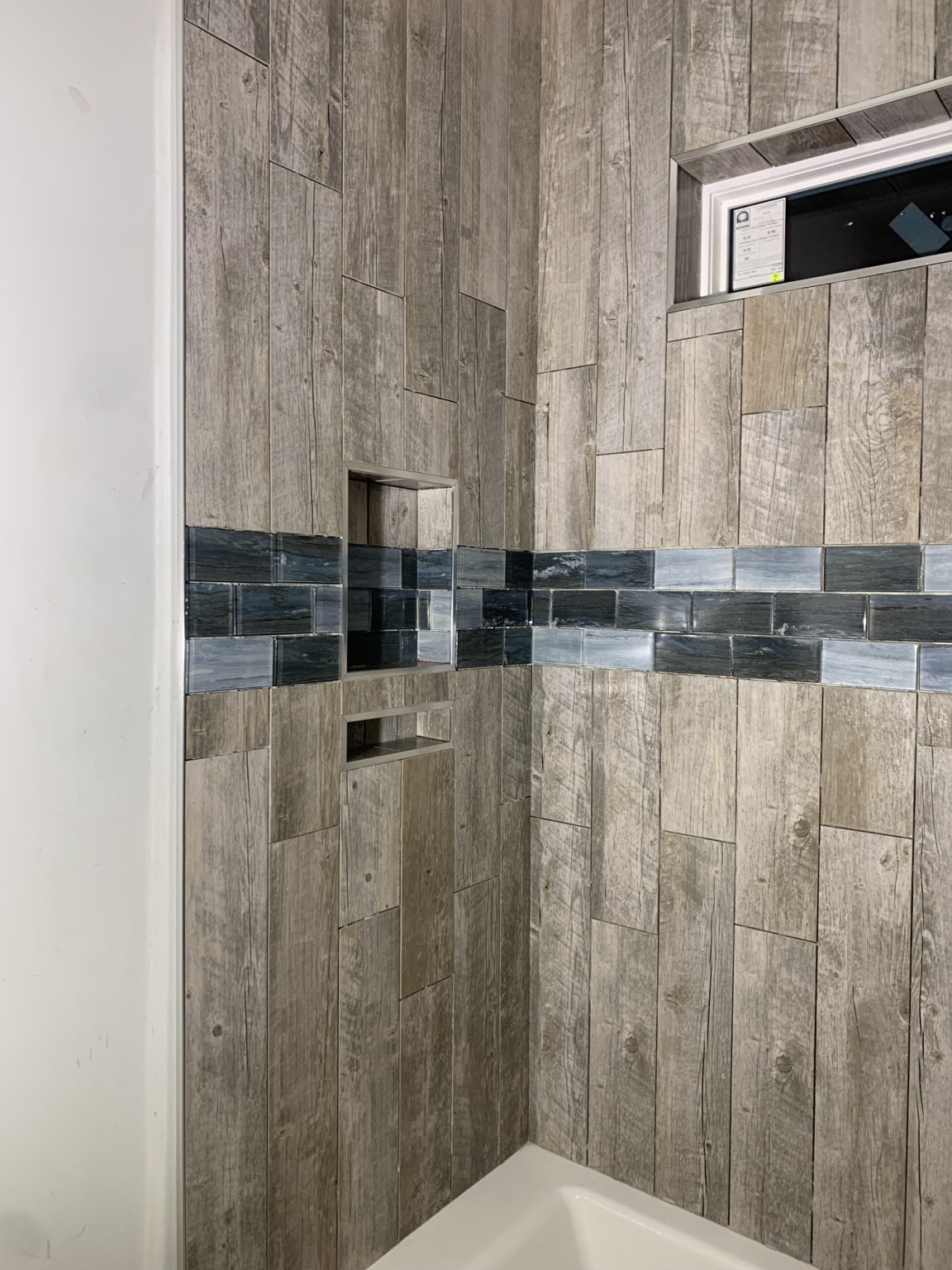 Wood-look tile shower with a dark horizontal accent band and two recessed niches